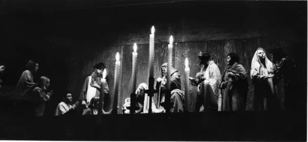 Actors perform a Christmas scene in front of candlelight